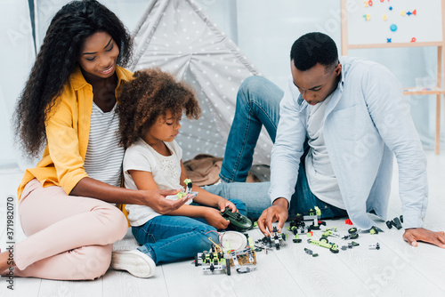 african american parents sitting on floor with daughter near plastic toys