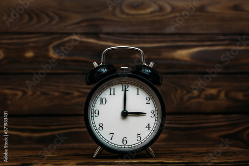 Clock on a wooden background. The clock shows the time of three o'clock in the afternoon. The clock shows the time of three o'clock in the morning. An image of a retro clock showing 03:00 pm/am. 
