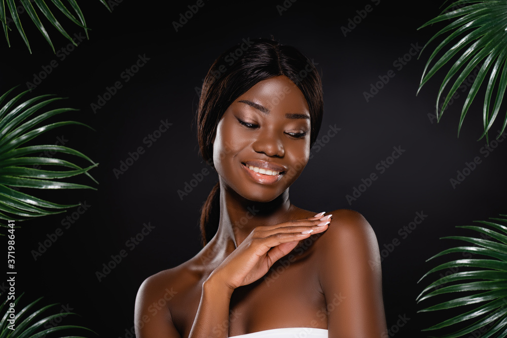 african american woman touching body near green palm leaves isolated on black african american woman touching body near green palm leaves isolated on black