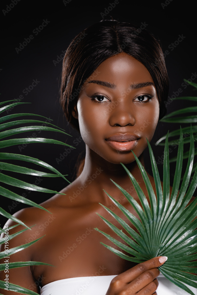 african american woman near green palm leaves isolated on black african american woman near green palm leaves isolated on black