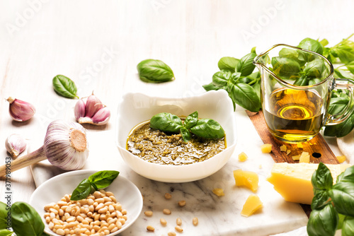 Bowl with pesto and fresh basil, garlic, parmesan cheese, pine nuts and olive oil on marble board. Kitchen wooden table with Italian sauce