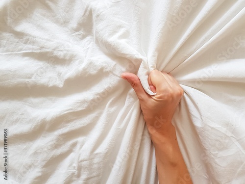 Close up sexy woman hand pulling and squeezing white sheets in ecstasy in bed. Orgasm on white bed. Sex and erotic concept.