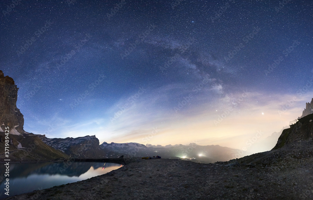Landscape of beautiful mountains area and lake with clear fresh water in Alps. Gorgeous mountain ridge with high rocky peaks, milky way with shining stars in dark sky. Panoramic view