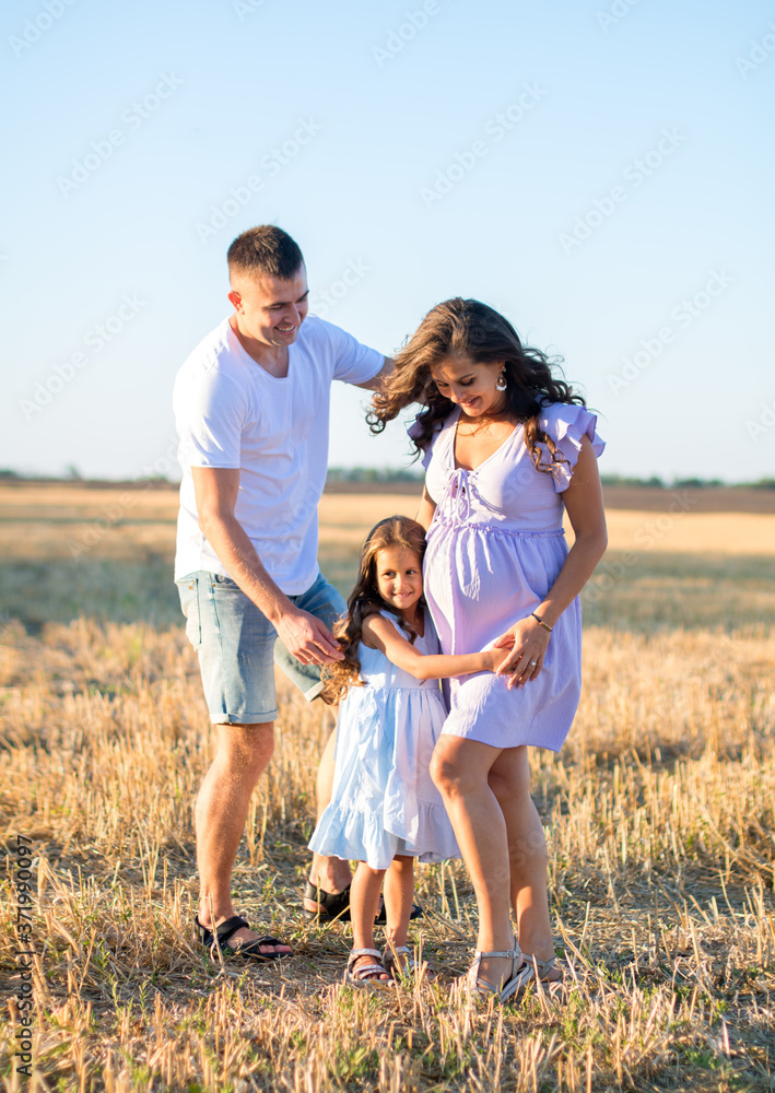 happy young family on the field, pregnant wife and a little girl hugs with father, wind turbines on the background happy young family on the field, pregnant wife and a little girl hugs with father, wind turbines on the background