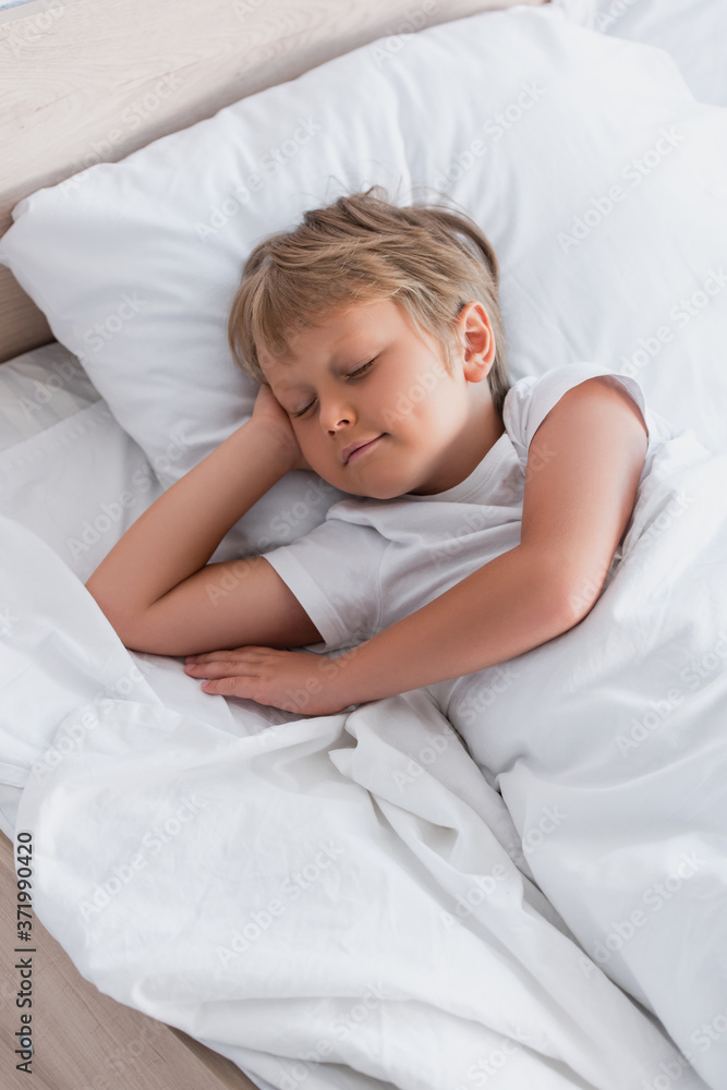 top view of boy sleeping on white bedding in morning top view of boy sleeping on white bedding in morning
