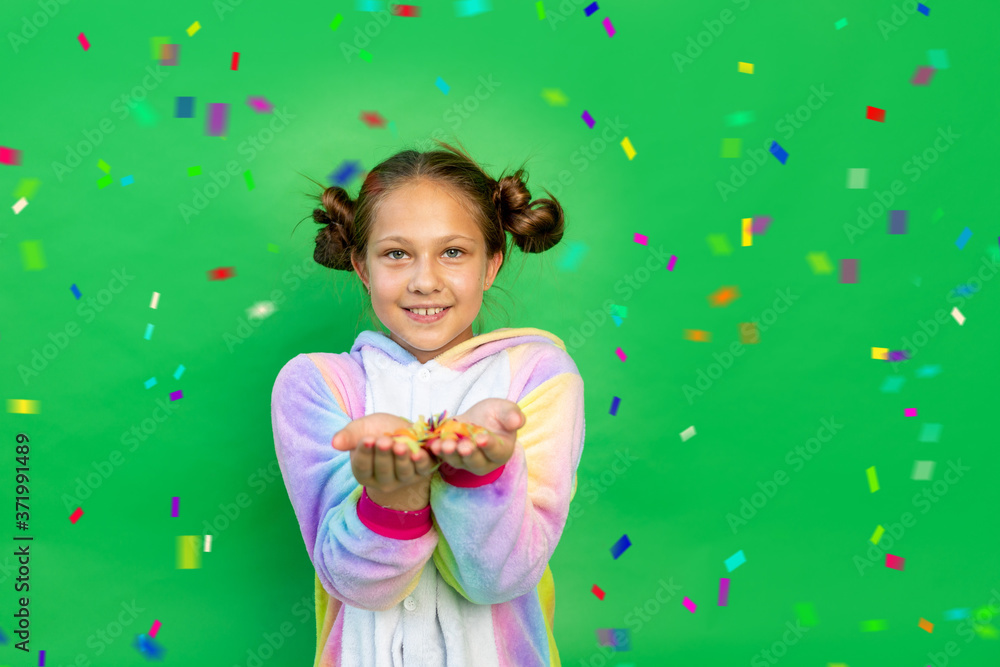 a little girl on a green isolated background in a bright suit blows away a streamer. Space for text. The concept of a holiday, Birthday and sales