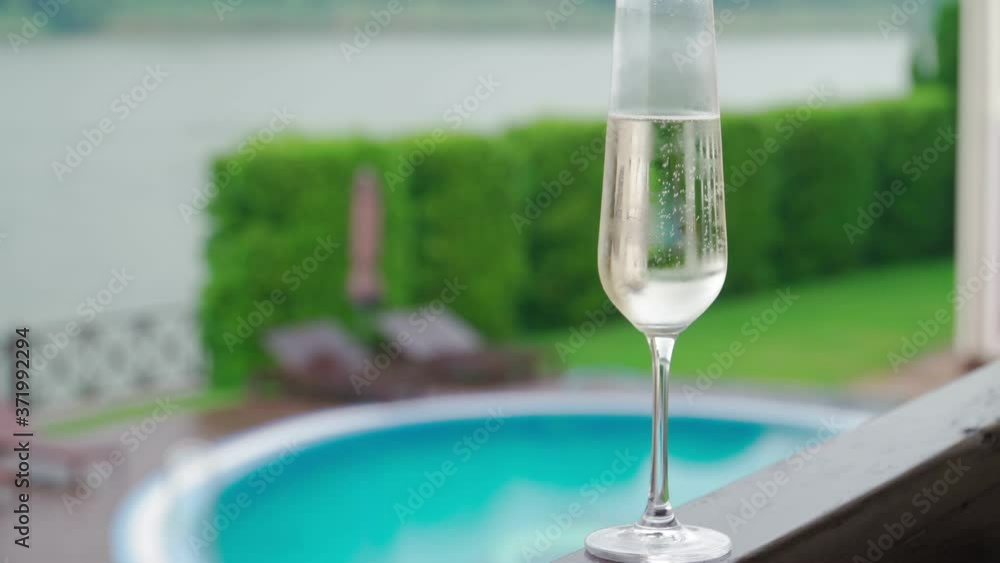 White champagne or prosecco glass against poolside at luxury resort hotel during vacation Close-up. Refreshing alcohol drink. Slow motion White champagne or prosecco glass against poolside at luxury resort hotel during vacation Close-up. Refreshing alcohol drink. Slow motion