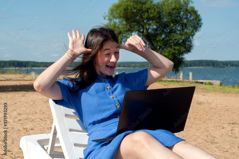girl greeting during videocall on laptop sitting in on the beach. Freelancer and blogger participates in Videoconference