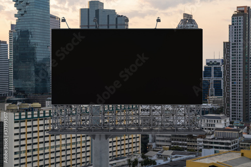 Blank black road billboard with Bangkok cityscape background at sunset. Street advertising poster, mock up, 3D rendering. Front view. The concept of marketing communication to promote or sell idea.