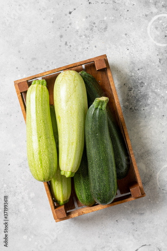Obraz na płótnie Raw zucchini. Zucchini in a wooden box on a light gray table. Top view with space for text. Zucchini crop w salonie