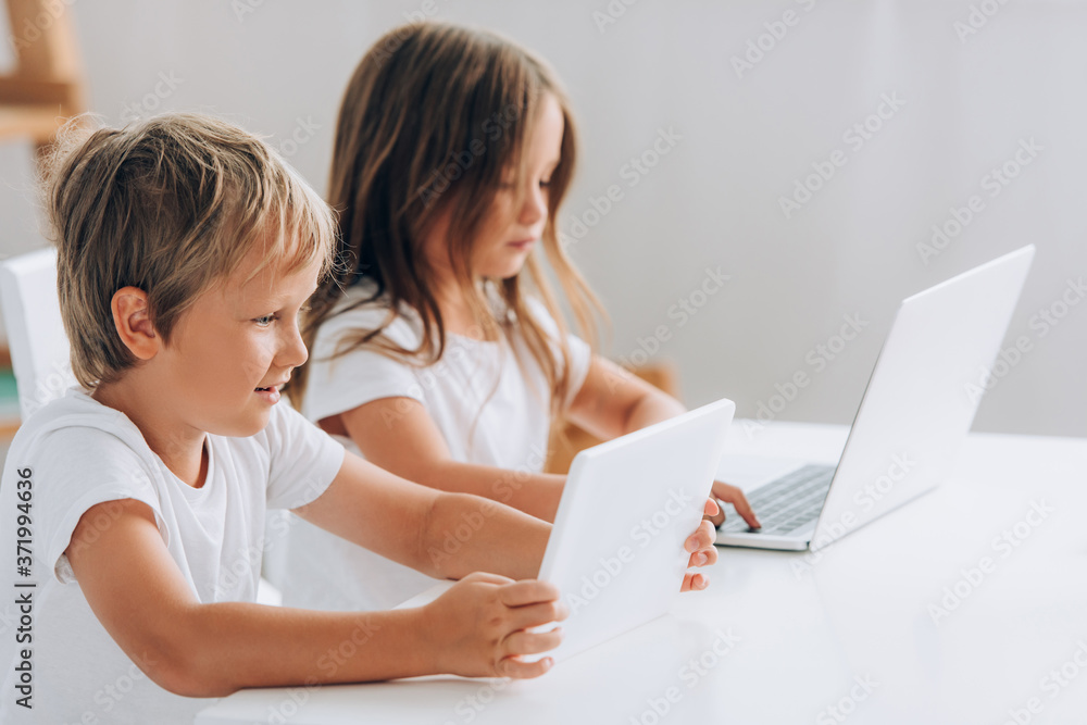 selective focus of brother and sister using laptops while sitting at table together selective focus of brother and sister using laptops while sitting at table together