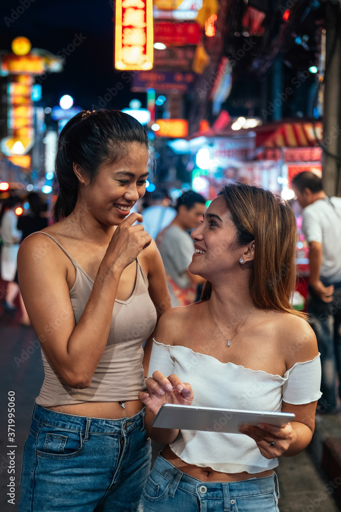 Girls in Bangkok at night looking at digital tablet stock photo Girls in Bangkok at night looking at digital tablet stock photo