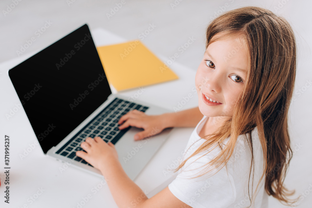 high angle view of girl looking at camera while using laptop with blank screen high angle view of girl looking at camera while using laptop with blank screen