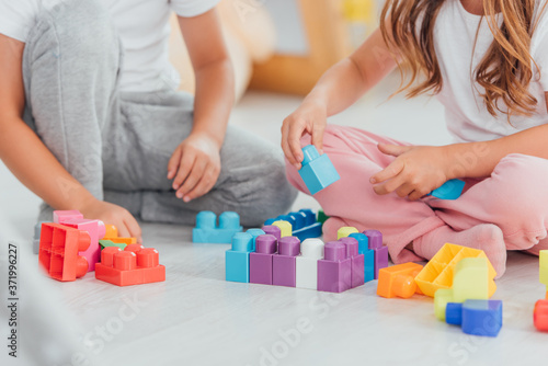 cropped view of children playing with building blocks while sitting on floor in pajamas