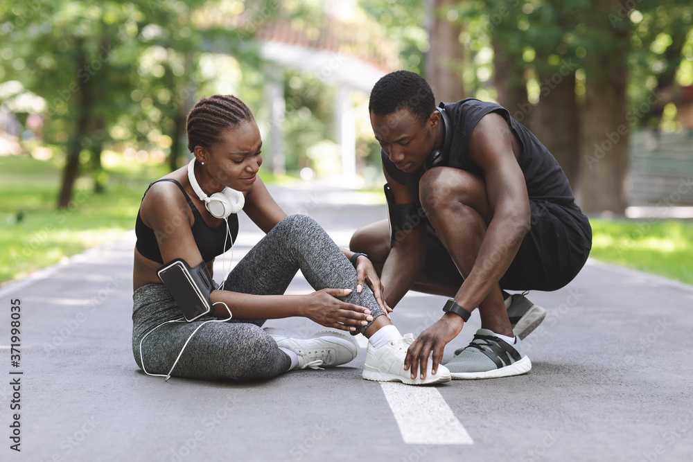 Jogging Injuries. Black Guy Helping Girlfriend Suffering From Sprained Ankle After Running Jogging Injuries. Black Guy Helping Girlfriend Suffering From Sprained Ankle After Running