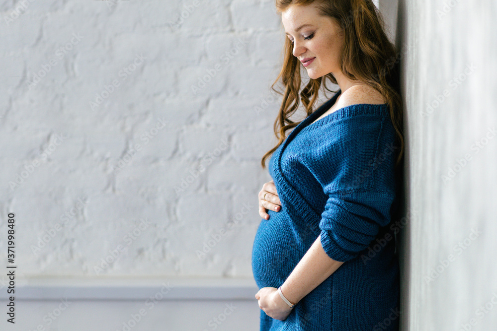 30 weeks pregnant woman wearing a blue bodycon dress stays by the white wall. Going on maternity leave, planning pregnancy, preparing for childbirth 30 weeks pregnant woman wearing a blue bodycon dress stays by the white wall. Going on maternity leave, planning pregnancy, preparing for childbirth