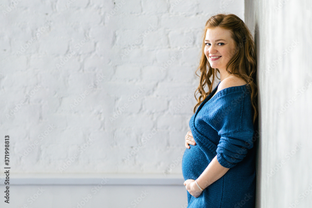 30 weeks pregnant woman wearing a blue bodycon dress stays by the white wall. Going on maternity leave, planning pregnancy, preparing for childbirth