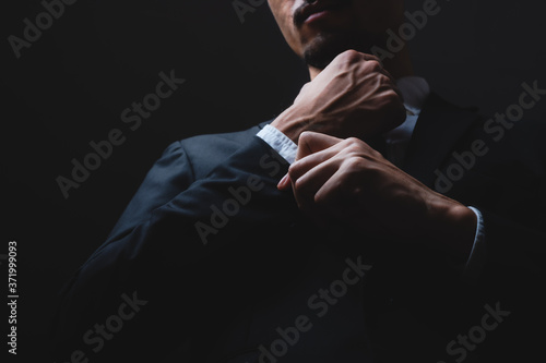 handsome confident businessman wearing and adjusting the black suit