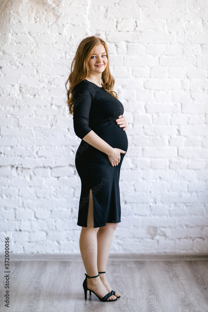 30 weeks pregnant pretty woman wearing a black bodycon dress. Planning pregnancy, preparing for childbirth. Full-length shot