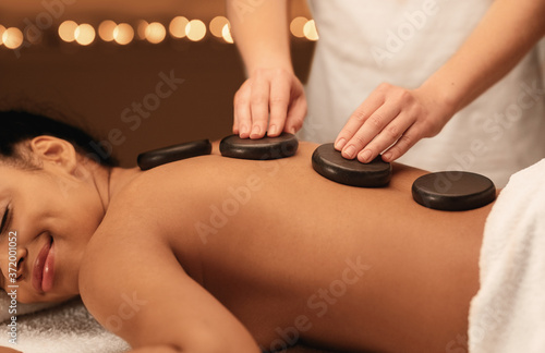 Masseuse hands applying hot stones on black woman back