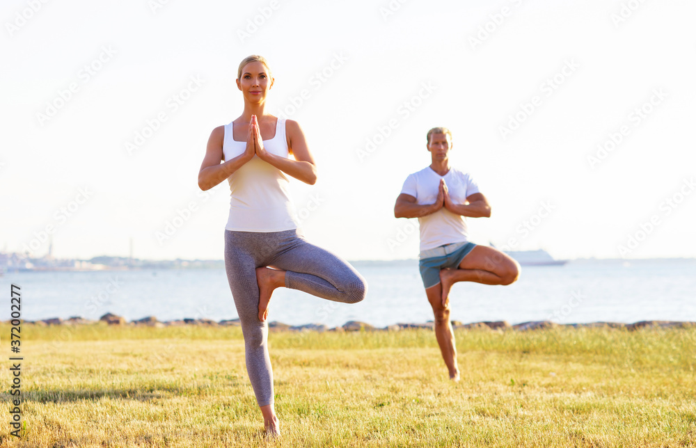 Fit man and beautiful woman practicing yoga outdoor on the grass. Stretching exercise in the sunset. Sport, fitness, health care and lifestyle concepts. Fit man and beautiful woman practicing yoga outdoor on the grass. Stretching exercise in the sunset. Sport, fitness, health care and lifestyle concepts.