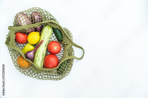String green bag with various fresh vegetables on white background. Zero waste concept, fresh vegetables in reusable net bags.
