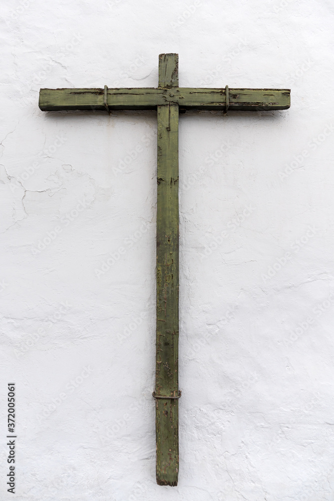 Altes verwittertes Kreuz aus Holz an einer weißen Wand, befestigt mit Bügeln aus Metall