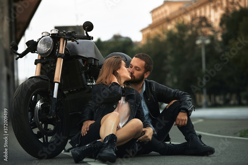 Beautiful biker couple in love are sitting on the road next to motorcycles in the city