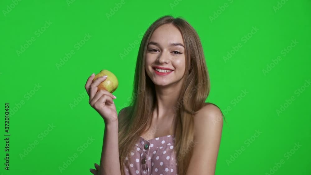 Smiling girl wearing summer dress smiling and holding green apple