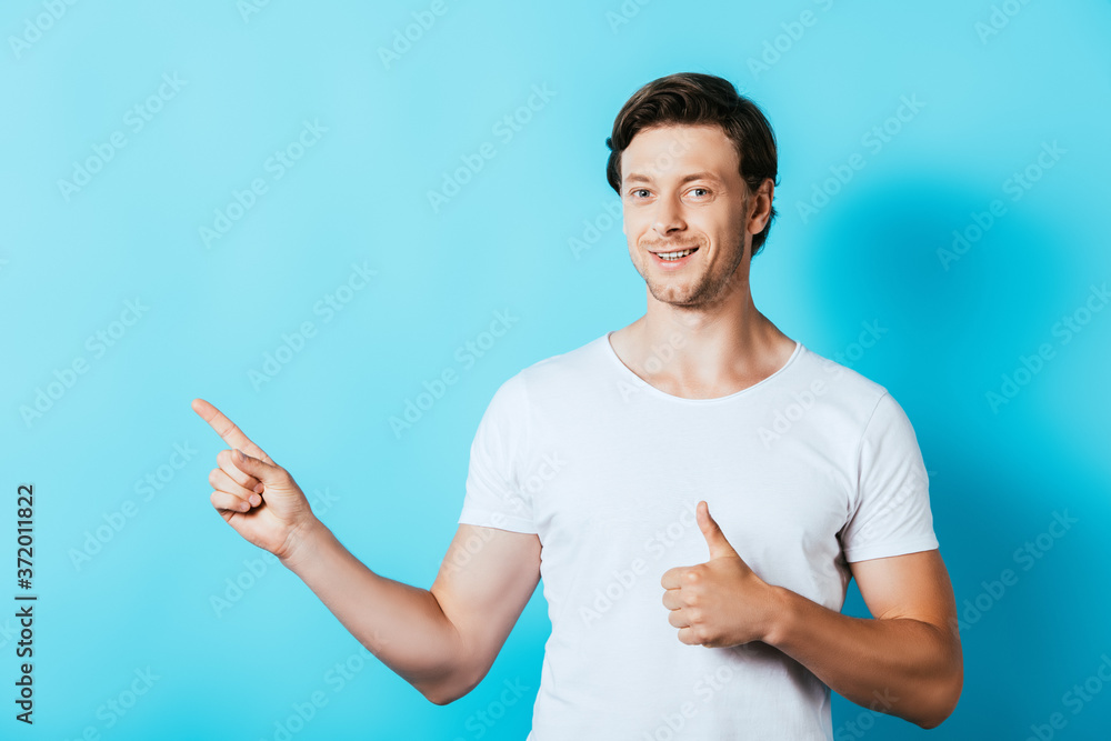 Young man in white t-shirt pointing with finger and showing like gesture on blue background Young man in white t-shirt pointing with finger and showing like gesture on blue background