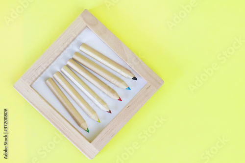 Colored pencils in a wooden frame on a yellow background. Copy space - concept of education  child development  back to school  creativity.