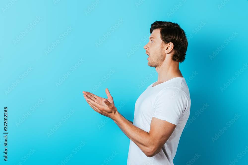 Side view of excited man pointing with hands and looking away on blue background Side view of excited man pointing with hands and looking away on blue background