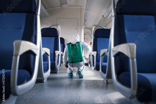 Public transportation healthcare. Man in white protection suit disinfecting and sanitizing subway train interior to stop spreading highly contagious coronavirus or COVID-19.