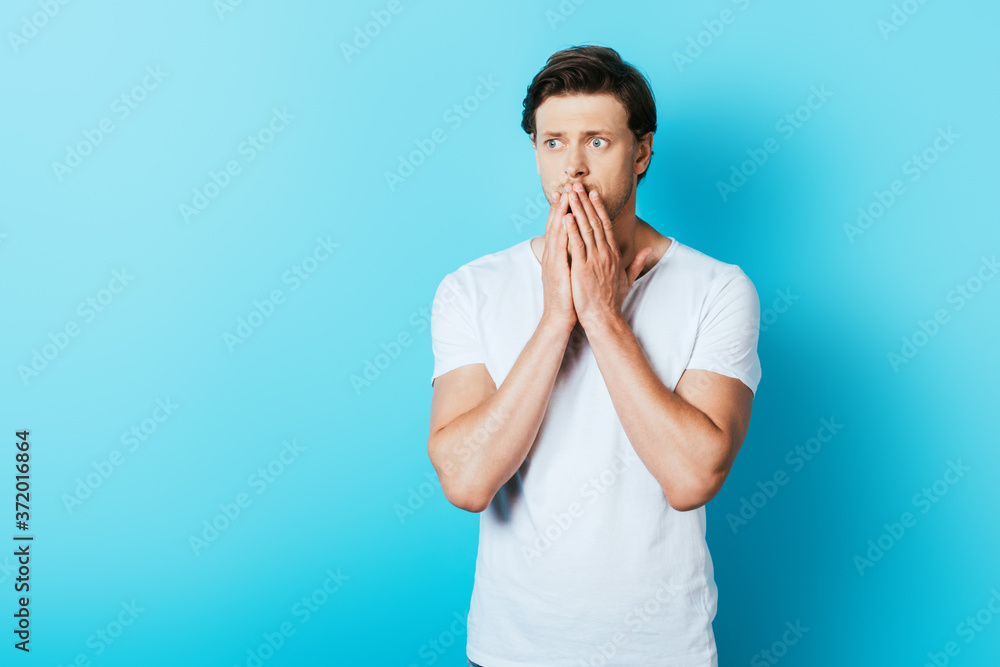 Sad man with hands near mouth looking away on blue background Sad man with hands near mouth looking away on blue background