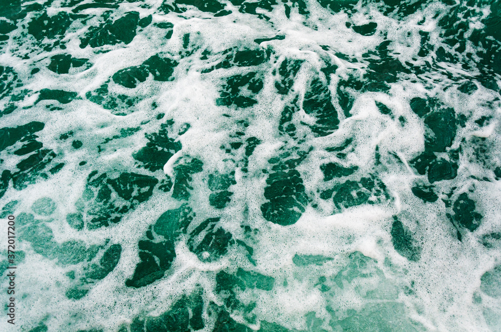 Dark turquoise sea water with white foam texture on the surface. Background image.