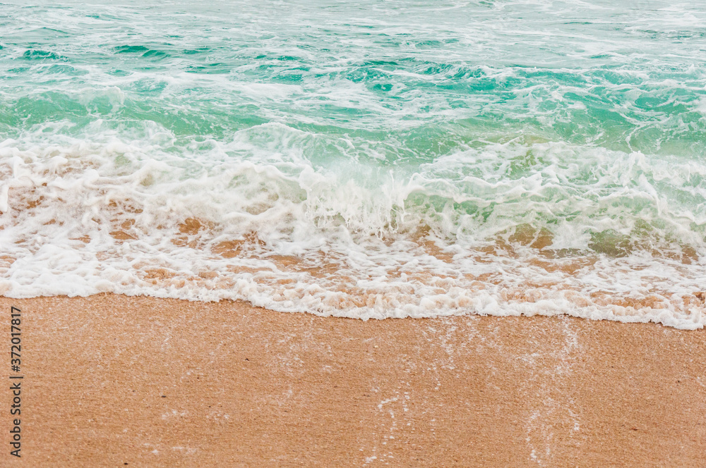 The beach with the waves coming across the sand. Predominant blue, green and yellow colors.