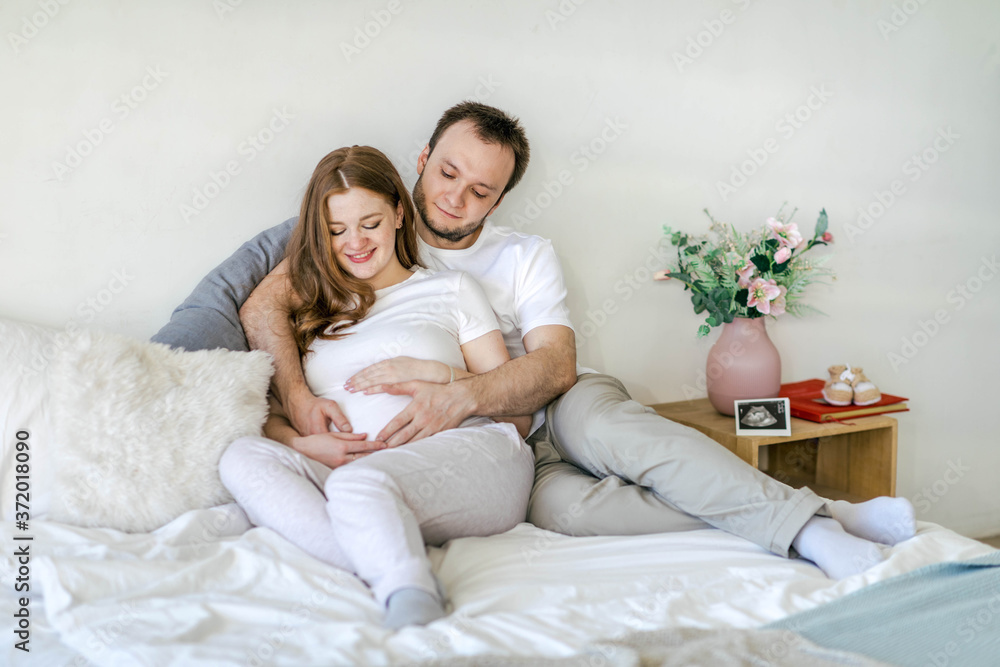Family waiting for the baby. Husband and pregnant wife in a bright interior hug and smile. Pregnancy planning and preparation for childbirth