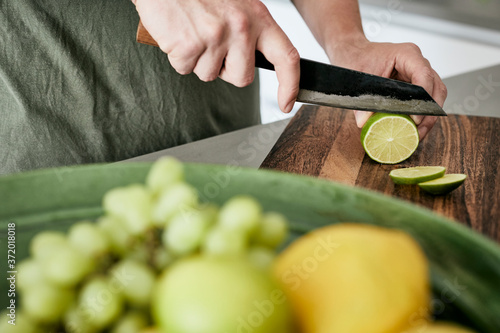 Mann, der eine Limette auf einem Holzbrett in Scheiben schneidet photo