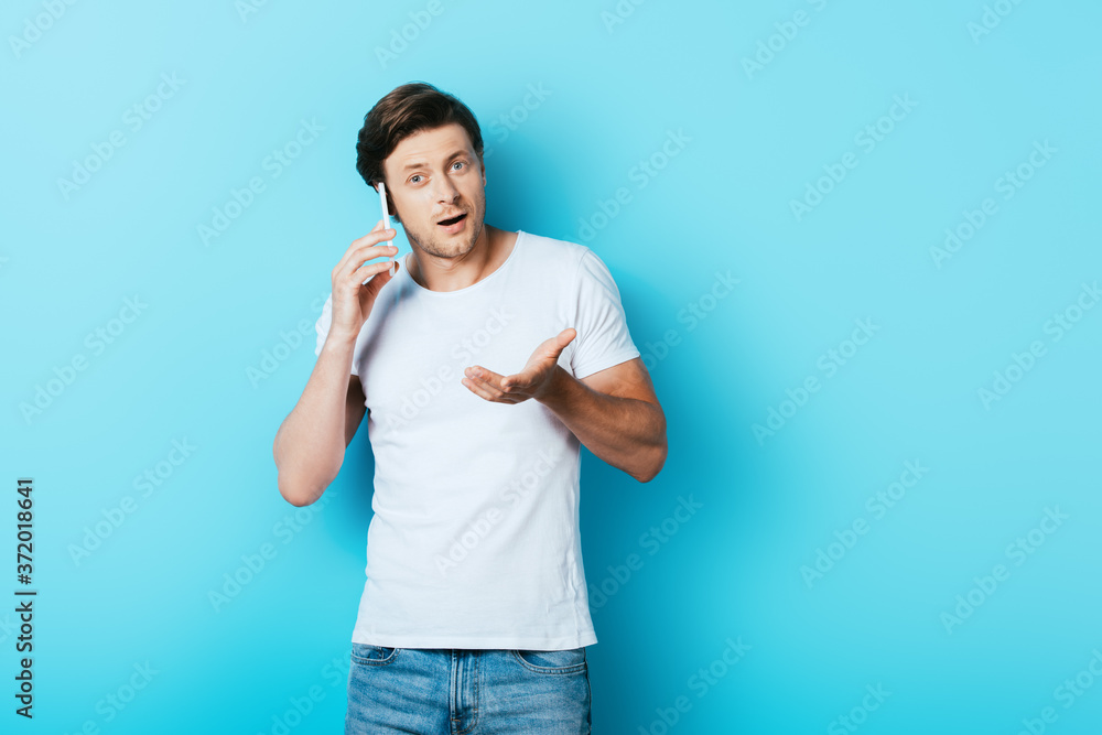 Young man pointing with hand while talking on smartphone on blue background Young man pointing with hand while talking on smartphone on blue background