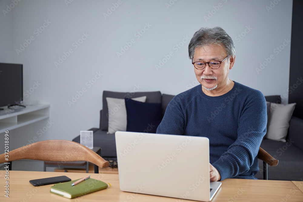 部屋の中でパソコンを操作するシニアの男性 部屋の中でパソコンを操作するシニアの男性