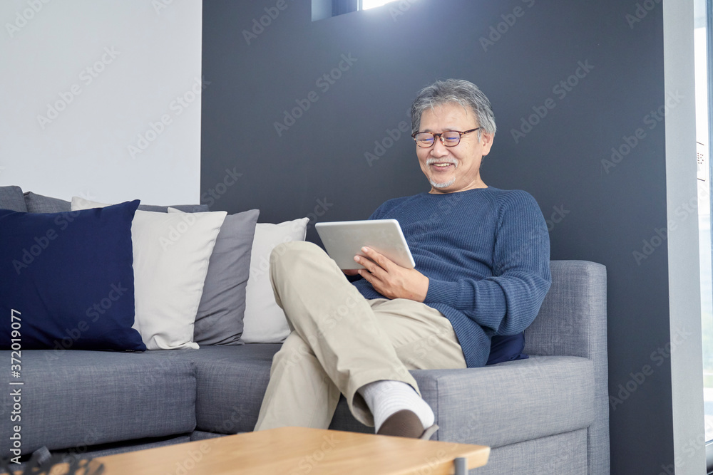 ソファーでくつろぎながらタブレットを操作するシニアの男性 ソファーでくつろぎながらタブレットを操作するシニアの男性