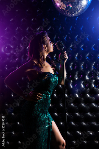 Young woman singing with microphone against dark background
