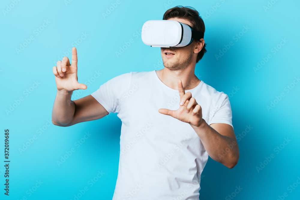 Young man pointing with fingers while using virtual reality headset on blue background Young man pointing with fingers while using virtual reality headset on blue background