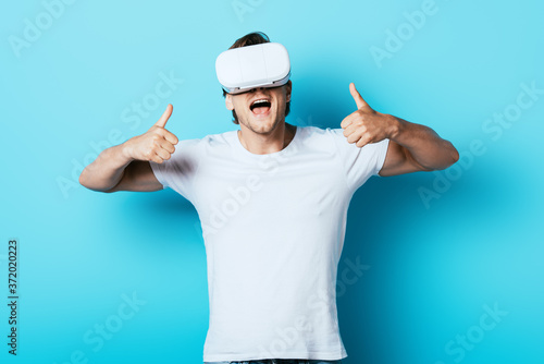 Young man in vr headset showing thumbs up on blue background