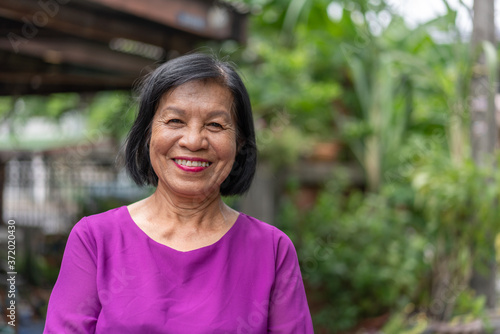 Smiling Asian elderly woman looking at camera standing outside at home