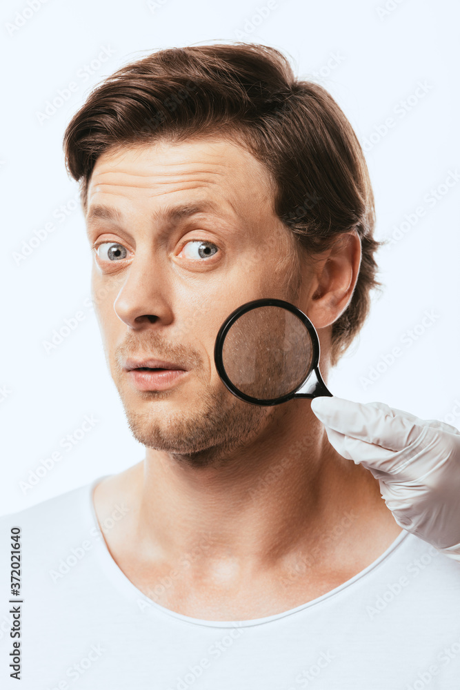 Dermatologist in latex glove holding loupe near shocked patient isolated on white Dermatologist in latex glove holding loupe near shocked patient isolated on white