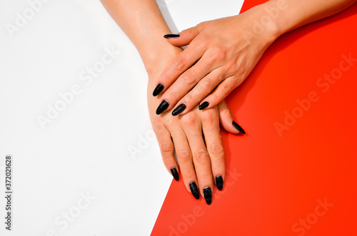 Stylish trendy female black manicure. Beautiful old woman s hands on white and red background