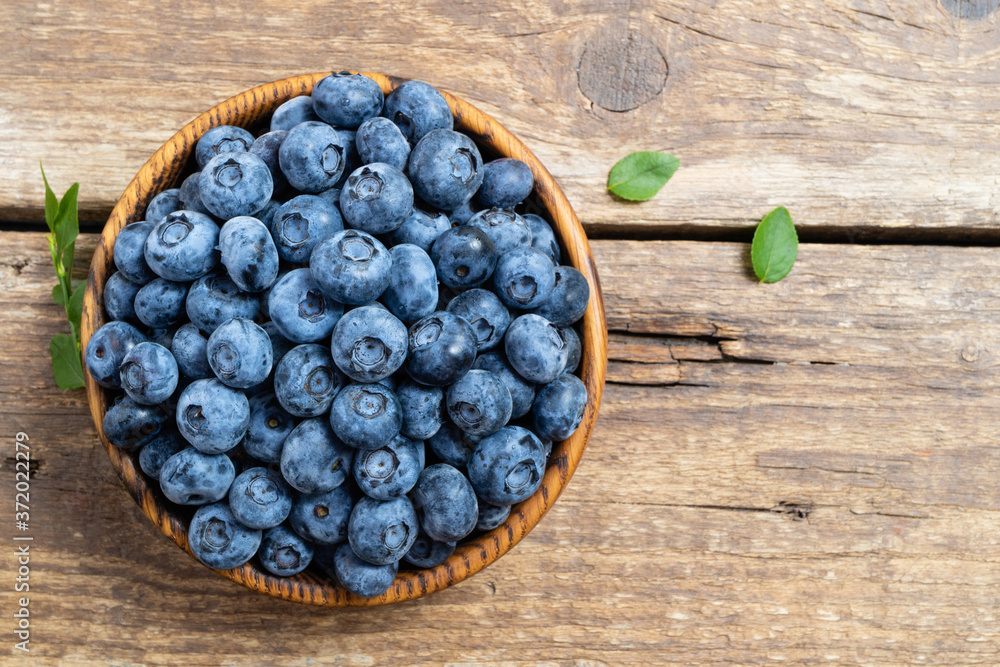 Fresh blueberry in wooden bowl. Juicy and fresh blueberries with green leaves on rustic table. Concept blueberry antioxidant for healthy eating and nutrition. Copy space, top view Fresh blueberry in wooden bowl. Juicy and fresh blueberries with green leaves on rustic table. Concept blueberry antioxidant for healthy eating and nutrition. Copy space, top view