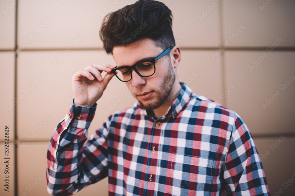 Handsome young man in trendy shirt and eyewear posing on wall background outdoors , smart male student dressed in stylish outfit thinking about education touching new spectacles for vision protection Handsome young man in trendy shirt and eyewear posing on wall background outdoors , smart male student dressed in stylish outfit thinking about education touching new spectacles for vision protection