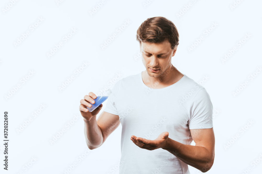 Young man holding bottle of lotion and looking at hand isolated on white Young man holding bottle of lotion and looking at hand isolated on white